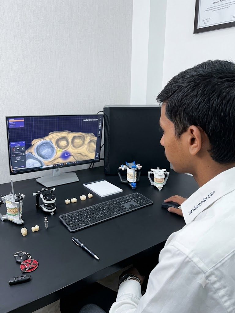 A technician designing a crown on screen, with articulated models and finished units on the bench beside him